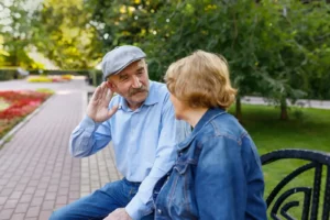 Older couple sitting on a bench talking with the men making a sign to the woman to speak louder