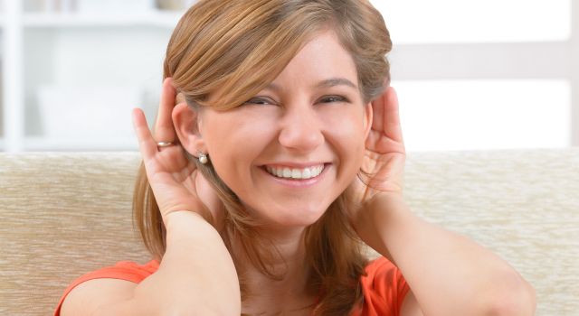 smiling woman holding her hands up to her ears