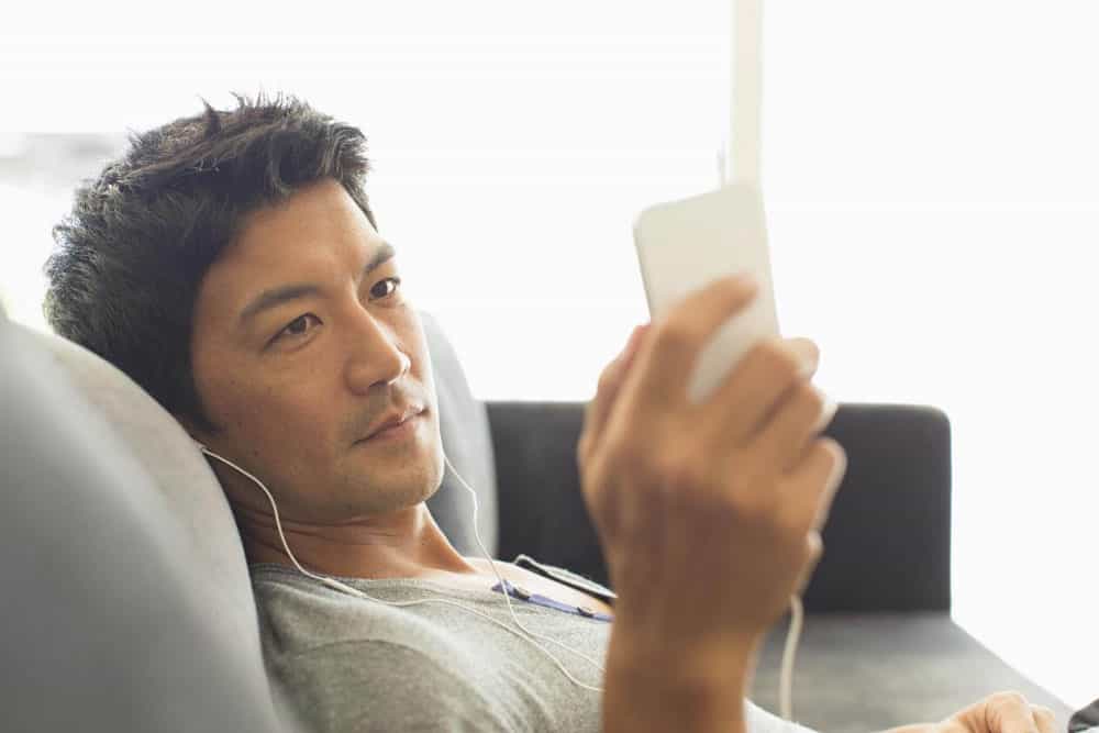 Man-listening-to-music-with-headphones-on-smart-phone-on-sofa