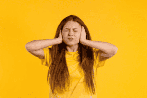 a young woman with red hair on an orange background covering her ears and closing her eyes