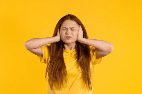 hyperacusis orange-min a young woman with red hair on an orange background covering her ears and closing her eyes