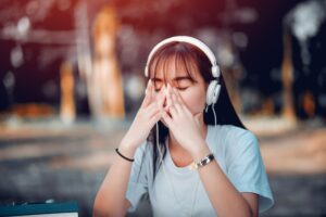 A young woman with headphones covering her face with her hands