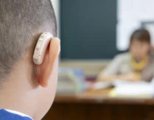 A closeup shot of a child wearing a hearing aid while sitting in a classroom.
