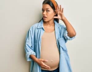 Pregnant woman with her hand behind her ear as if trying to hear better