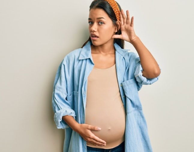 Pregnant woman with her hand behind her ear as if trying to hear better