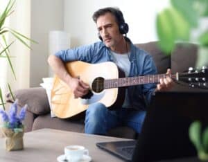 Man sitting on a couch with headphones playing the guitar.