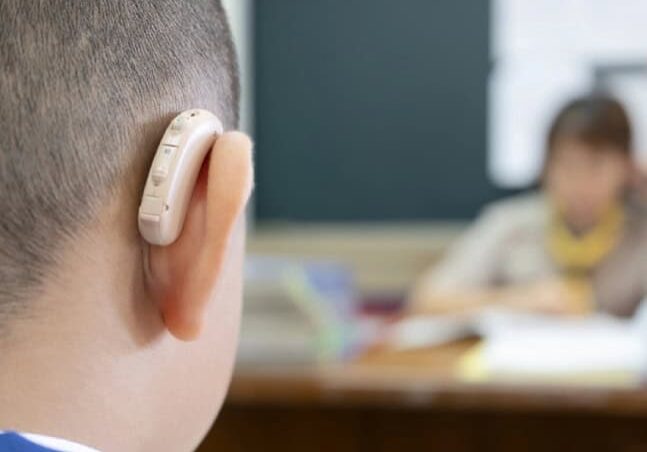 A closeup shot of a child wearing a hearing aid while sitting in a classroom.