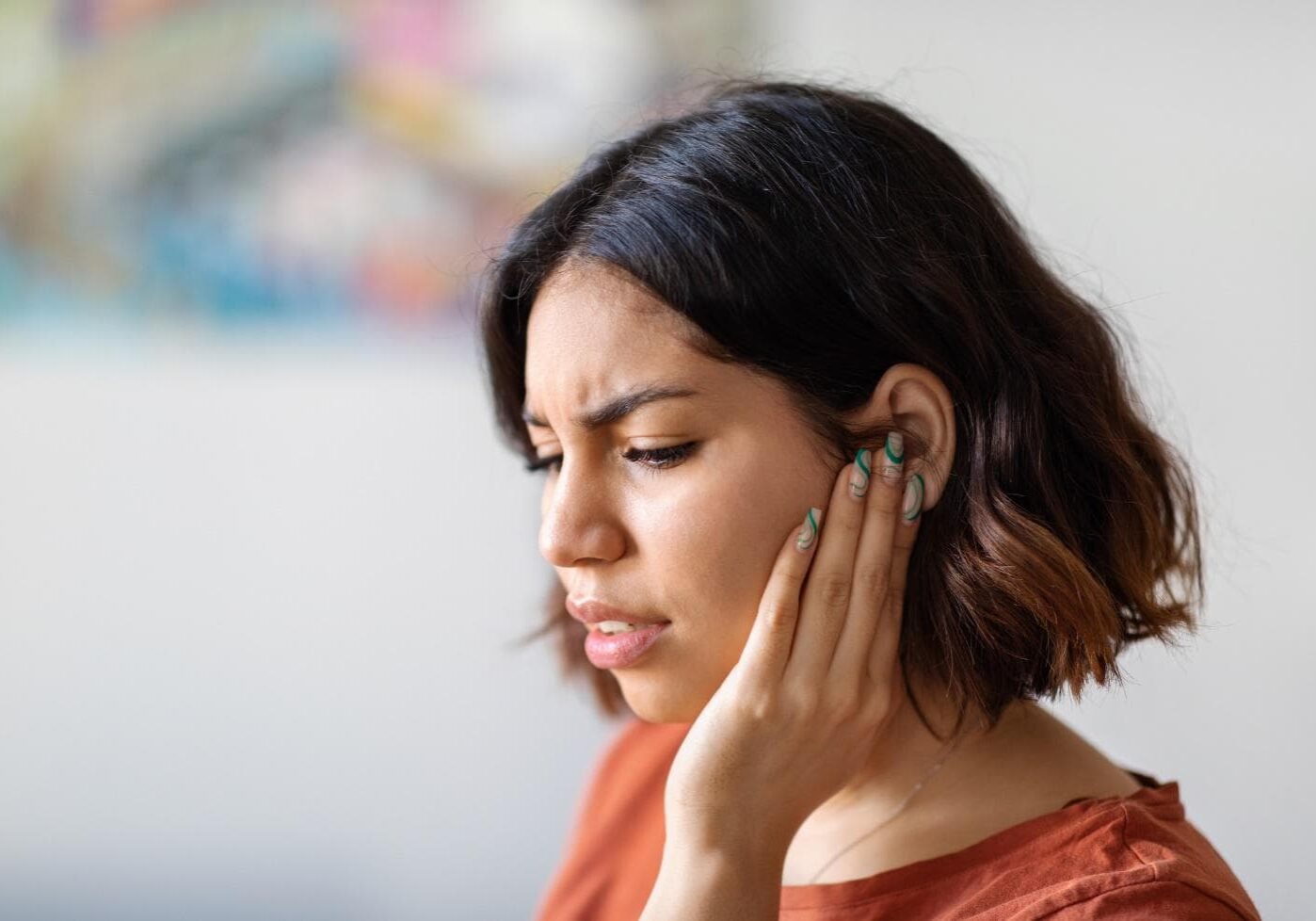 A woman holds a hand to the side of her face due to discomfort in her ear.