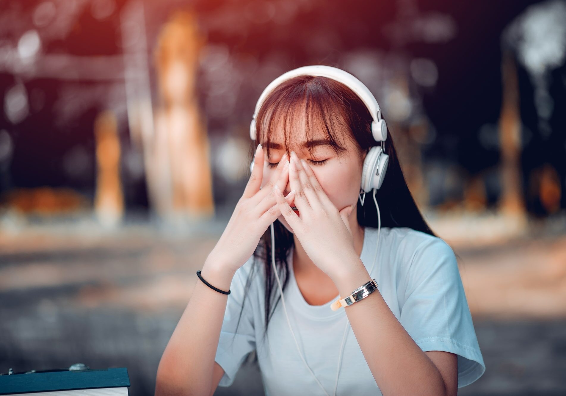 A young woman with headphones covering her face with her hands