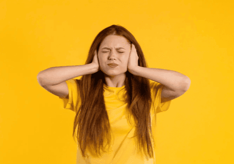 a young woman with red hair on an orange background covering her ears and closing her eyes