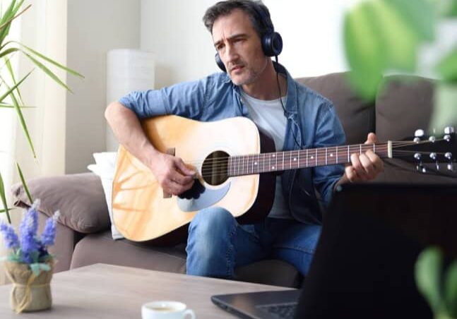 Man sitting on a couch with headphones playing the guitar.